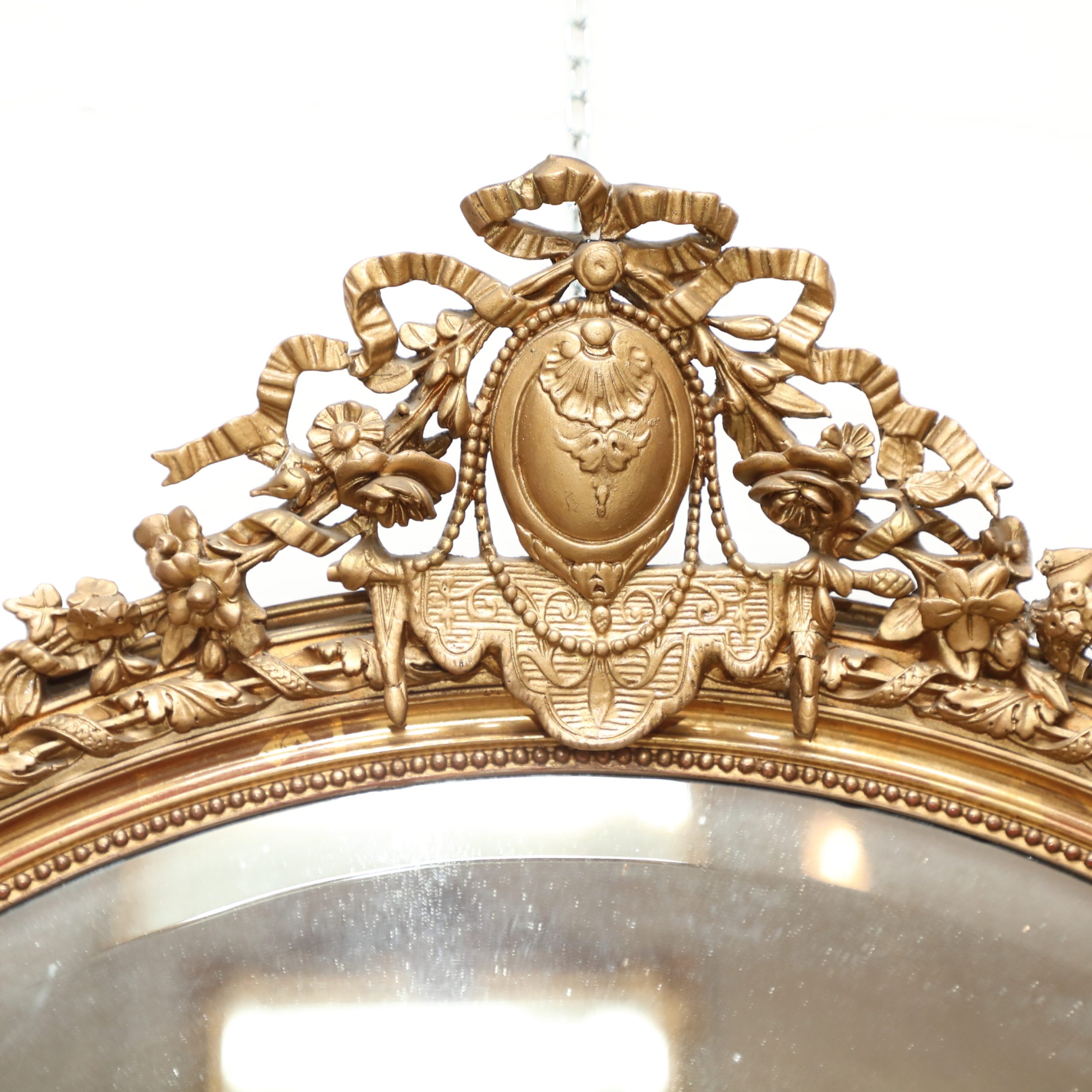 Oval wall mirror in gilded wood with coping with bow and various carvings, polished mirror - Wall Mirrors Oval wall mirror in gilded wood with coping with bow and various carvings, polished mirror - Wall Mirrors